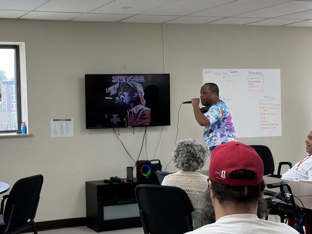 adult day care social fun philly Participant singing karaoke while others watch during a social activity session at Penn Village adult day care in Philadelphia